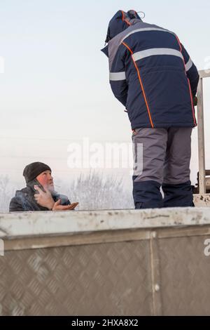 Porträt eines arbeitenden Assemblers in einer Jacke mit Kapuze und einem schwarzen Strickmütze, der auf einem Handy spricht Stockfoto