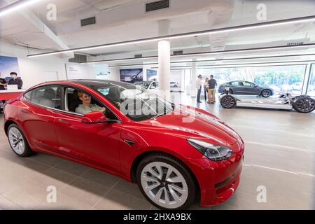 Die Dame des Tesla 3-Autosalons sitzt im 2022 Tesla Modell 3 hinter dem Steuer Stockfoto