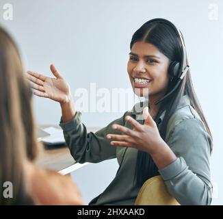 Ich habe versucht, dem Kunden das zu erklären. Aufnahme einer attraktiven jungen Verkäuferin, die mit einem Kollegen im Büro sitzt und ein Headset trägt. Stockfoto