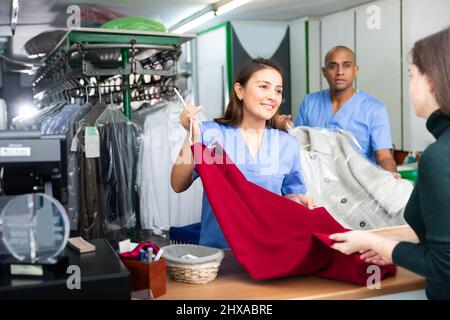 Gewöhnliche Frau und Mann, die mit dem Kunden in der modernen Wäscherei arbeiten Stockfoto