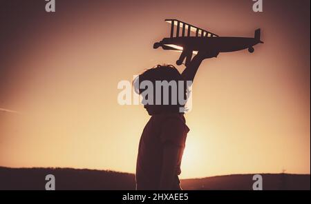 Kind träumt. Kind Pilot Flieger mit Flugzeug träumt von Reisen im Sommer in der Natur bei Sonnenuntergang. Stockfoto