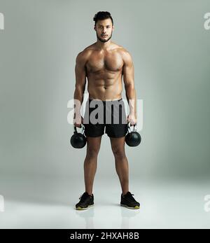 Es geht darum, in Form zu bleiben. Studio-Aufnahme eines jungen Mannes, der mit Kesselglocken vor grauem Hintergrund arbeitet. Stockfoto