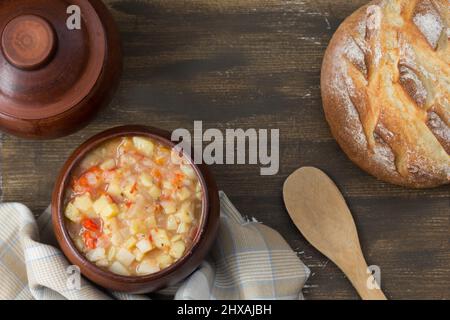 Draufsicht auf Kartoffeln und Gemüse Eintopf in Tontopf auf Holzhintergrund gekocht Stockfoto