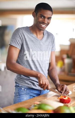 Mir hat meine eigene Kochshow nichts ausgemacht. Aufnahme eines gutaussehenden ethnischen Mannes, der Gemüse im Haus zubereitet. Stockfoto