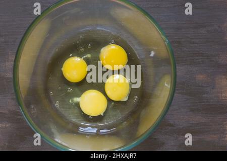 Vier rohe Eigelbe und weiße Hühnchen in Glasschüssel auf einem Holztisch Stockfoto