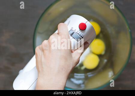Frau hält den Mixer in einer Glasschüssel mit Zucker und Eiern Stockfoto