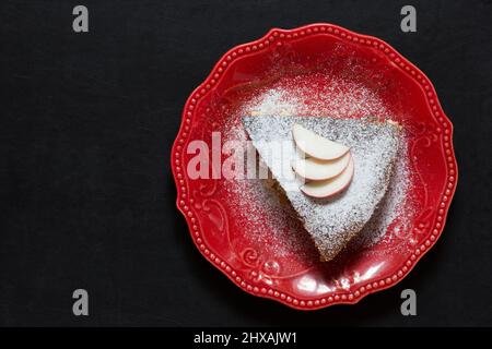 Draufsicht auf ein Stück Apfelkuchen auf roter Platte auf schwarzem Hintergrund Stockfoto