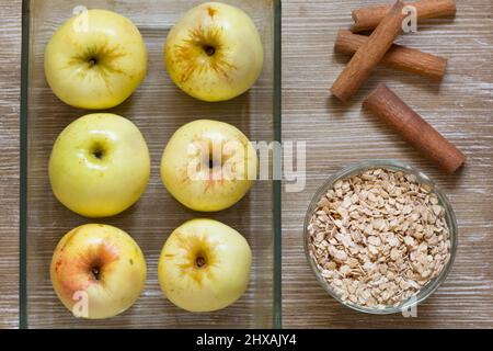 Draufsicht auf Äpfel Hafer Zimtstangen als Zutaten für gebackene Äpfel auf dem Holzhintergrund Stockfoto
