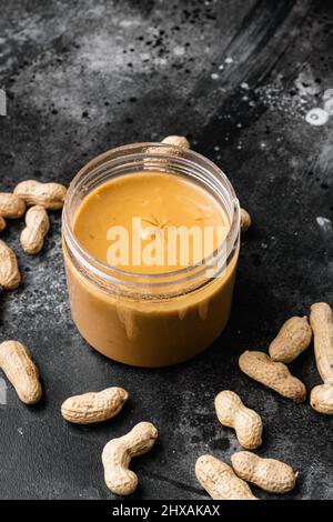 Glas mit Erdnussbutter mit Erdnussset, auf schwarzem dunklen Stein-Tischhintergrund, mit Platz für Text Stockfoto