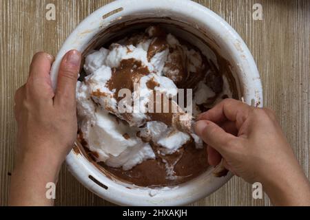 Hand einer Frau, die vor dem Backen den Teig mit geschältem Weiß in der Schüssel rührt Stockfoto