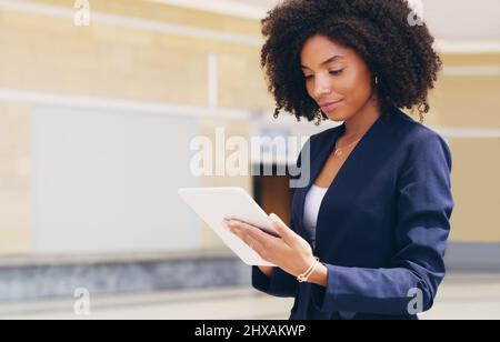 Meine E-Mails durchgehen. Eine kurze Aufnahme einer attraktiven jungen Geschäftsfrau, die tagsüber im Büro allein steht und ein Tablet benutzt. Stockfoto