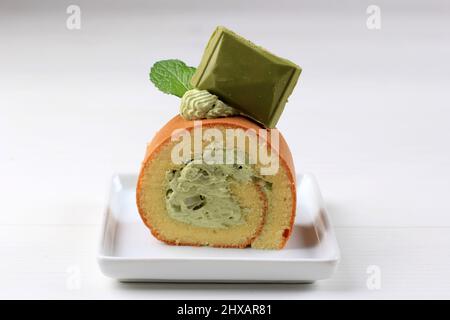 Grüner Tee-Rollkuchen mit Matcha-Schokolade auf der Oberseite, serviert auf weißem Kuchen, weißer Tisch Stockfoto