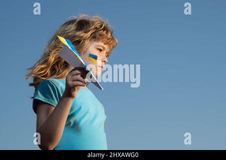 Schließen Sie den Himmel über der Ukraine Banner. Keine Flugzone über der Ukraine. Militärflugzeug mit Raketen und Bomben. Zeichen der ukrainischen Flagge auf Kinderwange. Stockfoto