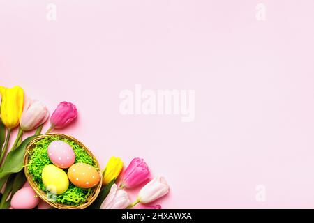 Osterkarte. Eier in einem Korb und Blumen Tulpen auf einem rosa Hintergrund. Stockfoto