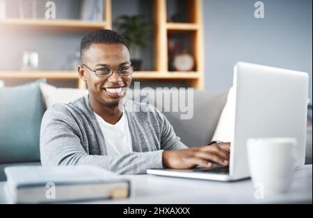 Ich bleibe in Verbindung, sodass ich nichts vermisse. Porträt eines glücklichen jungen Mannes, der einen Laptop benutzt, während er sich zu Hause entspannt. Stockfoto