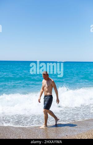 Attraktiver junger Mann mit einem schönen Körper in Shorts Spaziergänge entlang der sandigen Küste und genießen Sommerurlaub Stockfoto