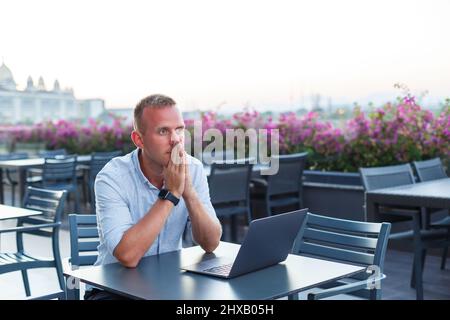 Erfolgreicher junger männlicher Geschäftsmann, der im Urlaub mit einem Laptop arbeitet. Er trägt ein Hemd und weiße Shorts. Arbeiten Sie außerhalb des Büros, Freiberufler Stockfoto