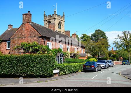 Reihe eines traditionellen roten Backsteingebäudes mit der All Saints Church auf der Rückseite entlang der Church Lane, Kings Bromley, Staffordshire, England, Großbritannien, Europa. Stockfoto