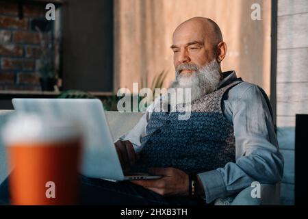 Älterer Mann mit einem Glas Wein mit seinem Laptop. Stockfoto