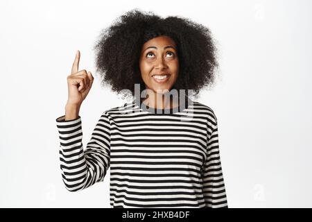 Nahaufnahme Porträt einer lächelnden afroamerikanischen Dame, die Informationen zeigt, die Finger nach oben zeigt, Ansage vorführt, weißer Hintergrund Stockfoto