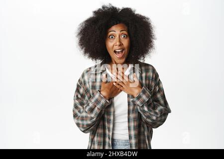 Porträt einer überraschten und verblüfften schwarzen Frau, die fasziniert keuchte, aufgeregt auf die Kamera schaute und beeindruckt auf weißem Hintergrund stand Stockfoto