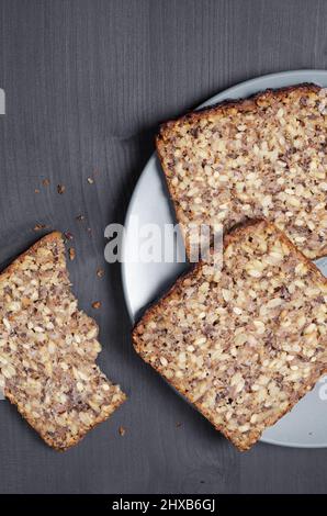 Brotscheiben mit verschiedenen Samen in einer grauen Platte auf schwarzem Holzhintergrund, Draufsicht Stockfoto