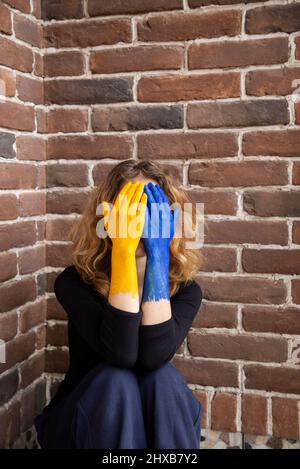 Unverkennbare verzweifelte Frau bedeckte ihr Gesicht mit den in den Farben der ukrainischen Flagge gemalten Händen, dem Krieg in der Ukraine. Russische Aggression, t Stockfoto