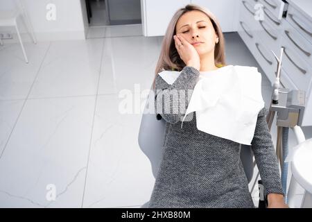 Ein junges kaukasisches Mädchen in legerer Kleidung berührt ihren Mund mit ihrer Hand mit einem schmerzhaften Gesichtsausdruck aufgrund von Zahnschmerzen oder Zahnerkrankungen Stockfoto