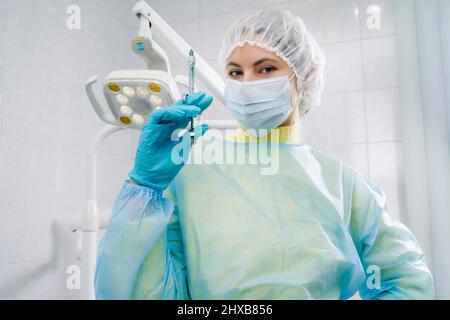 Ein maskierter Zahnarzt hält eine Injektionsspritze für einen Patienten im Büro. Stockfoto