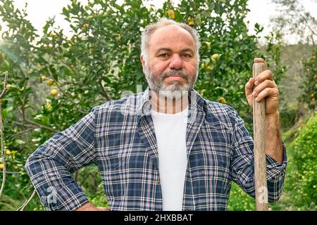 Porträt eines reifen bärtigen Gärtners, der im Obstgarten arbeitet. Pflege des Gartens. Gartenarbeit im Frühling. Saisonales Beschneiden von Bäumen. Stockfoto