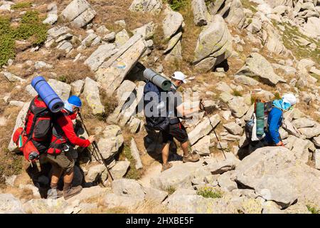 Drei männliche Wanderer in voller Sommerausrüstung, die zwischen Felsbrocken im Pirin Nationalpark und Naturschutzgebiet, Pirin Berg, Bulgarien, Balkan, Europa, hinuntergehen Stockfoto