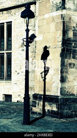 Eine altmodische elektrische Straßenlampe steht vor einer alten schmutzigen Wand und wirft ihren Schatten auf das Sandsteingebäude Stockfoto