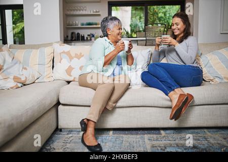 Im Sturm chatten. Aufnahme einer jungen Frau und ihrer Mutter, die beim Kaffee auf dem Sofa aufholen. Stockfoto