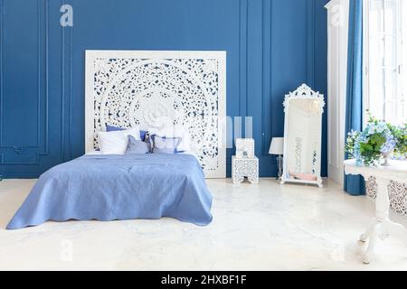 Wunderschönes, klassisches, sauberes, luxuriöses Schlafzimmer in Weiß und Dunkelblau mit Kingsize-Bett und schicken geschnitzten Möbeln. Helles, modernes, stilvolles Schlafzimmer und Wohnzimmer im minimalistischen Stil Stockfoto