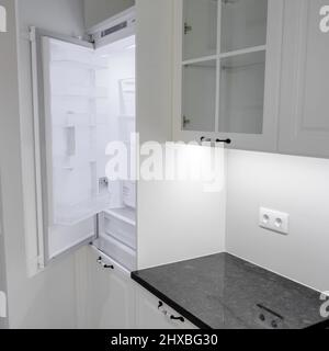 Seitenansicht moderne und elegante Küche mit weißen Schubladen und Schränken, Arbeitsplatte aus schwarzem Marmor und eingebautem Waschbecken mit silbernem Wasserhahn Stockfoto