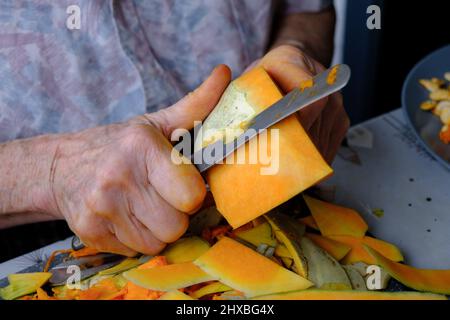 Alte Frau schneidet und Pillen gelben Kürbis, Kochen Kürbissuppe, Ruhestand Leben, selektive Konzentration Stockfoto