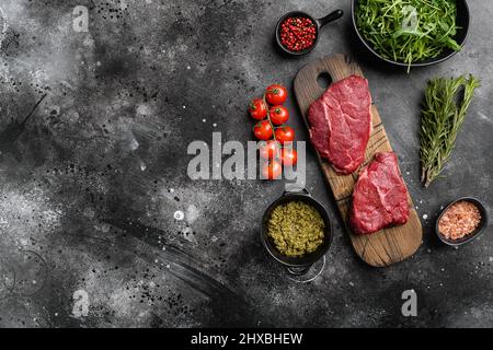 Steak-Set mit roher Mütze, auf schwarzem, dunklem Steintisch-Hintergrund, Draufsicht flach, mit Platz für Text Stockfoto