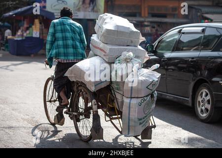 MANDALAY, MYANMAR - 12. JANUAR 2016: Nicht identifizierter Mann, der am 12. Januar 2016 in Mandalay, Myanmar, Waren mit dem Fahrrad transportiert Stockfoto