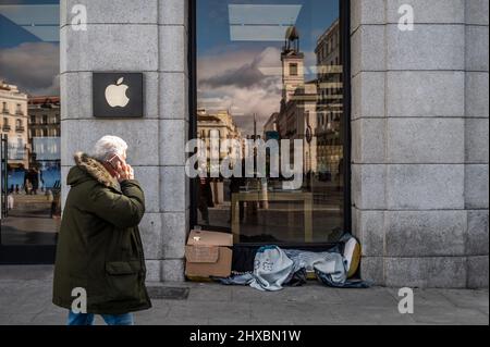 Ein Mann geht an einem Apple-Laden in der Innenstadt von Madrid vorbei, während ein Obdachloser unter Decken schläft Stockfoto