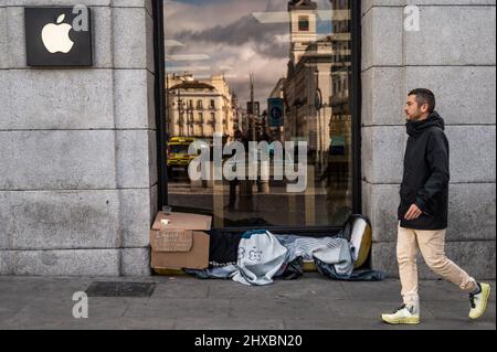 Ein Mann geht an einem Apple-Laden in der Innenstadt von Madrid vorbei, während ein Obdachloser unter Decken schläft Stockfoto