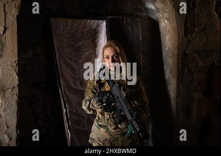 Kaukasische Frau in Armeeuniform, die ein Maschinengewehr hält und in der Nähe eines offenen Sarges steht. Stockfoto