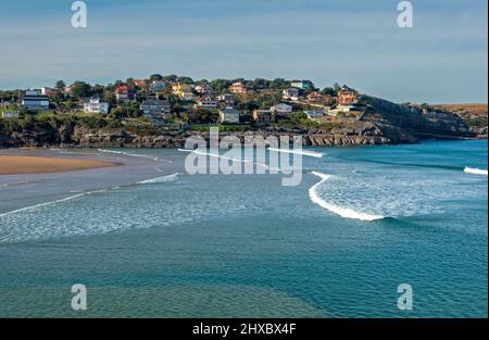 Wellen brechen am Strand Playa de la Arena mit Küstenhäusern in der Ferne in La Sorrozuela, Kantabrien, Spanien Stockfoto