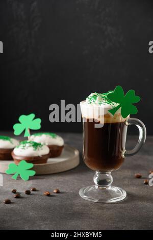 Irischer Kaffee in Glastasse und Cupcakes für den St. Patricks Day auf grünem Hintergrund. Vertikales Format. Nahaufnahme. Stockfoto