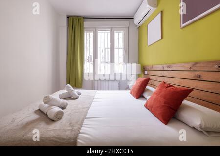 Schlafzimmer mit Kingsize-Bett in der Ferienwohnung mit Bettkopfteil aus Paletten und pistaziengrün gestrichenen Wänden, braunen Kissen und Rollhandtüchern Stockfoto