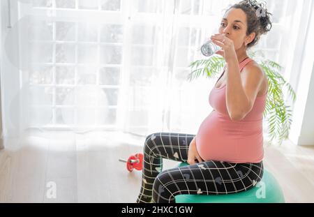 Schwanger junge Frau trinken aus einer Wasserflasche zu Hydrat nach dem Training. Konzept der Gesundheitsversorgung und Hydratisierung in der Schwangerschaft Stockfoto
