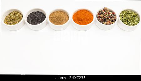 Verschiedene Arten von Gewürzen in verschiedenen Farben in Keramikschalen auf weißem Hintergrund isoliert verstreut, Ort für Text. Stockfoto