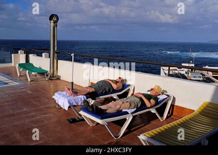 An Rentner, die auf Sonnenliegen auf einem Hoteldach auf Teneriffa schlafen. Stockfoto