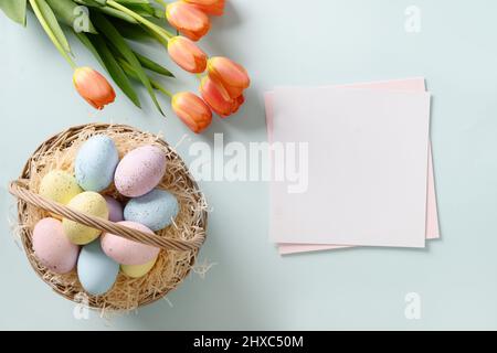 Osterkarte mit Eiern im Weidenkorb und Tulpen auf blauem Hintergrund. Ansicht von oben.Speicherplatz kopieren. Stockfoto