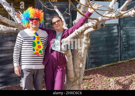 Glückliches Seniorenpaar, das sich für Halloween, Purim oder eine Geburtstagsfeier verkleidet hat. Lustige alte Mann in einem Clown Kostüm und glückliche ältere Frau mit Kristallen Gesicht Aufkleber Feier Purim jüdischen Feiertag. Stockfoto