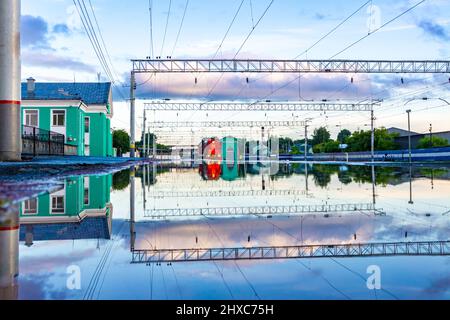 Nach einem heftigen Regen wird der Bahnsteig mit Wasser überflutet, das eine rote Diesellokomotive und Stationsausstattung und den Himmel reflektiert, selektiv fo Stockfoto